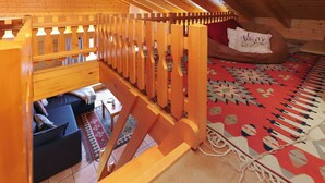 A wooden interior with a sloped ceiling, a wooden railing, a patterned rug, and a bed with a pillow. - Vacation home Lara by Interhome (Nendaz)