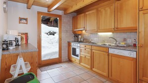 A kitchen with wooden cabinets, a stove, an oven, a sink, and a window with a view of snow outside. - Vacation home Lara by Interhome (Nendaz)