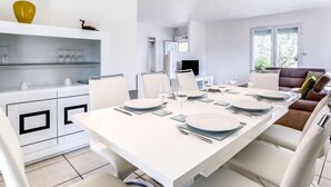 Een moderne eetruimte met een witte tafel voor vier personen, witte stoelen en een witte kast met glazen.