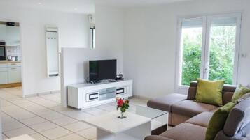 Ein modernes Wohnzimmer mit einer weißen Unterhaltungsecke, einem Flachbildfernseher, einem Glastisch und einem braunen Sofa mit grünen Kissen.