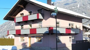 A multi-story building with a pink facade, balconies, and a snow-covered roof. - Apartment Heidi by Interhome (Kaltenbach)