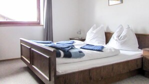 Een enkel bed met houten frame, een nachtkastje met lamp, een raam met gordijnen en een lijst met afbeelding aan de muur.