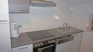 Een kleine keuken met een inbouwoven, een kookplaat, een spoelbak en een koffiezetapparaat.