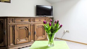 Een kamer met een houten kast, een flatscreen televisie aan de muur en een vaas met tulpen op een tafel.