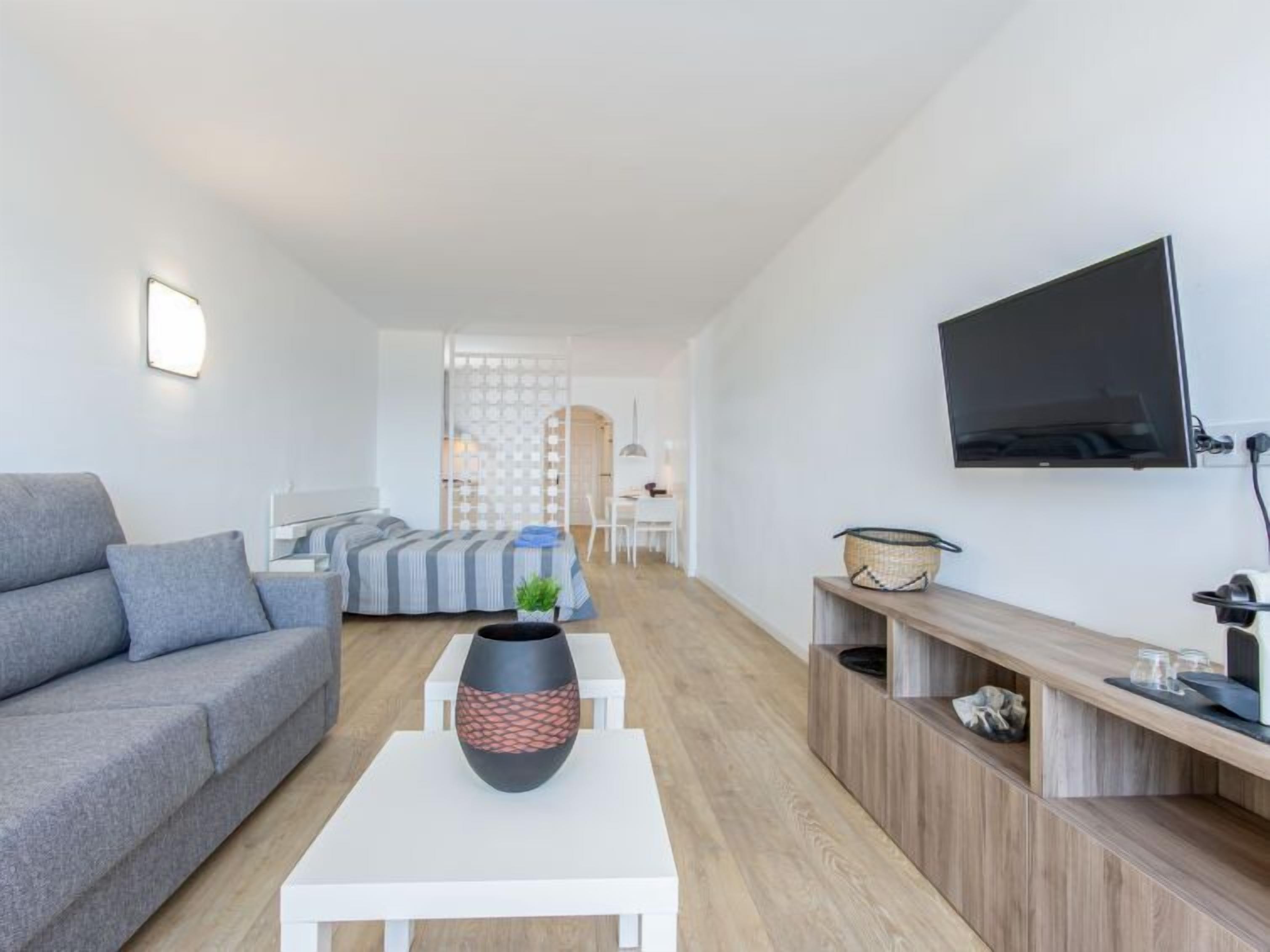 A modern living room with a grey sofa, a white coffee table, a TV mounted on the wall, and a wooden console table.