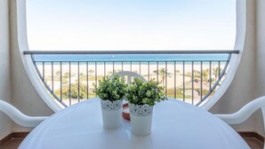 Un balcon donnant sur la plage, deux plantes en pot et une table blanche.