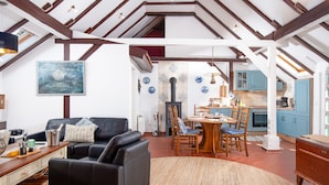 Uma sala de estar espaçosa com um sofá de couro preto, uma área de refeições com cadeiras de madeira e uma cozinha com armários azuis.