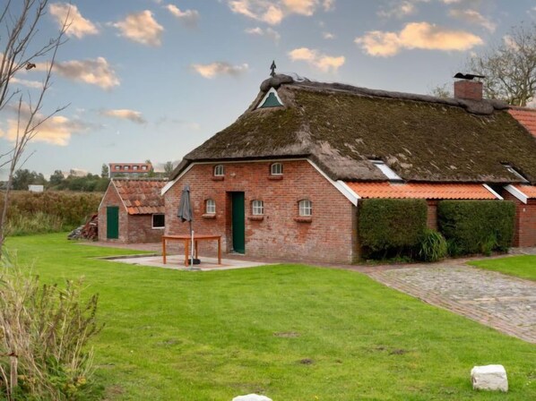 Une maison traditionnelle en briques, avec un toit de chaume, un petit jardin et un chemin en pierre.