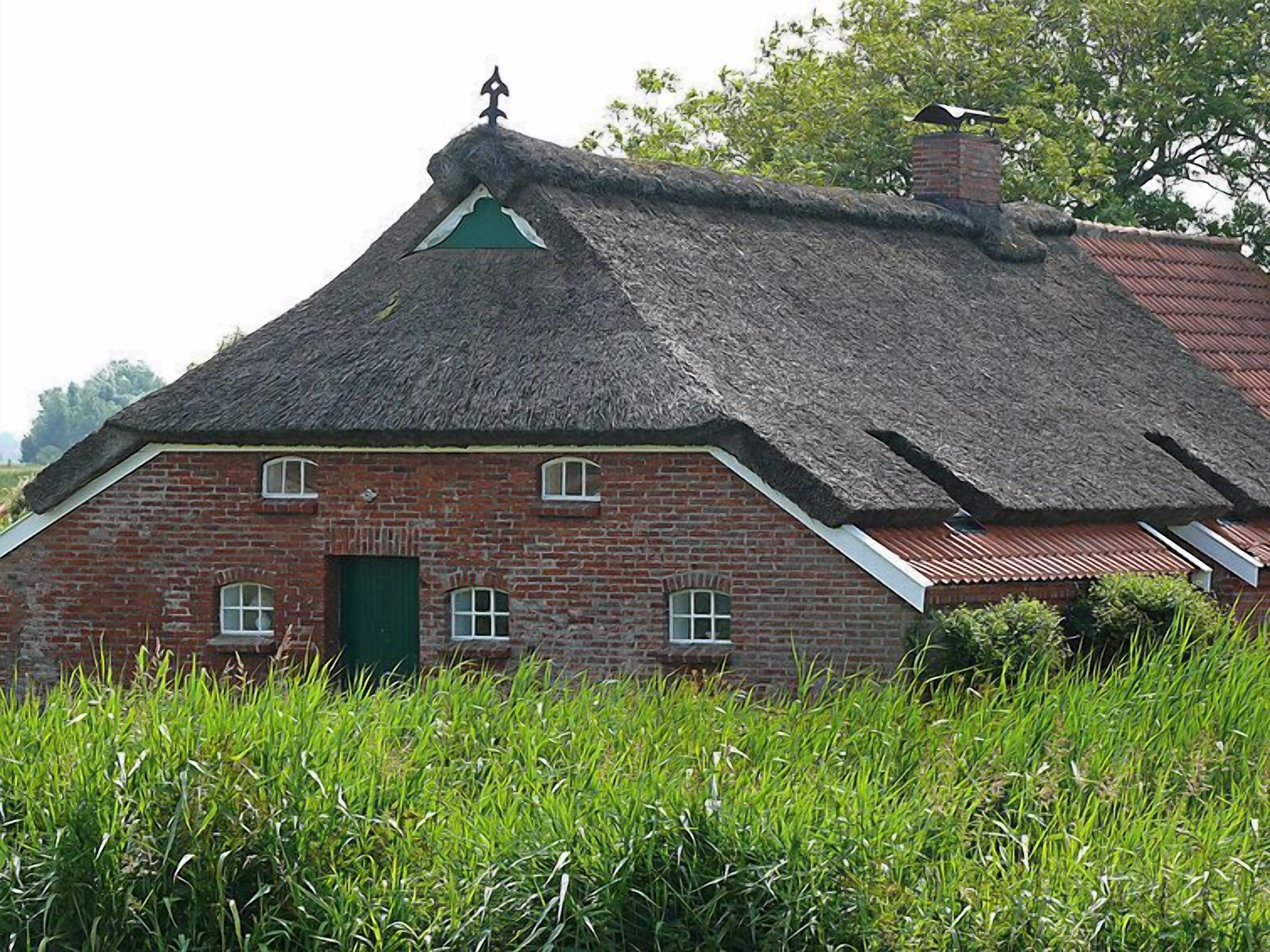 Ett traditionellt hus byggt av tegel med ett halmtak och en grön dörr.