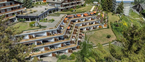 A modern hotel complex with multiple buildings, outdoor seating areas, and a mountainous backdrop.