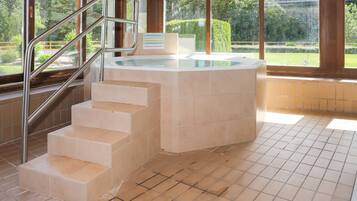 Un espace spa comprenant un jacuzzi, un escalier et une vue sur un jardin, visible à travers de grandes fenêtres.