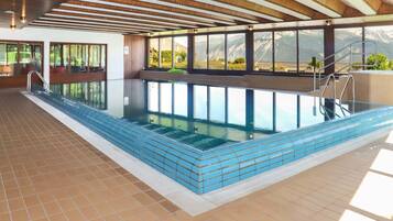Une piscine intérieure offrant une vue dégagée sur les montagnes grâce à de grandes fenêtres.
