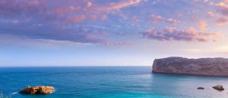Overlooking a serene coastal landscape with a prominent rock formation and sandy beach.