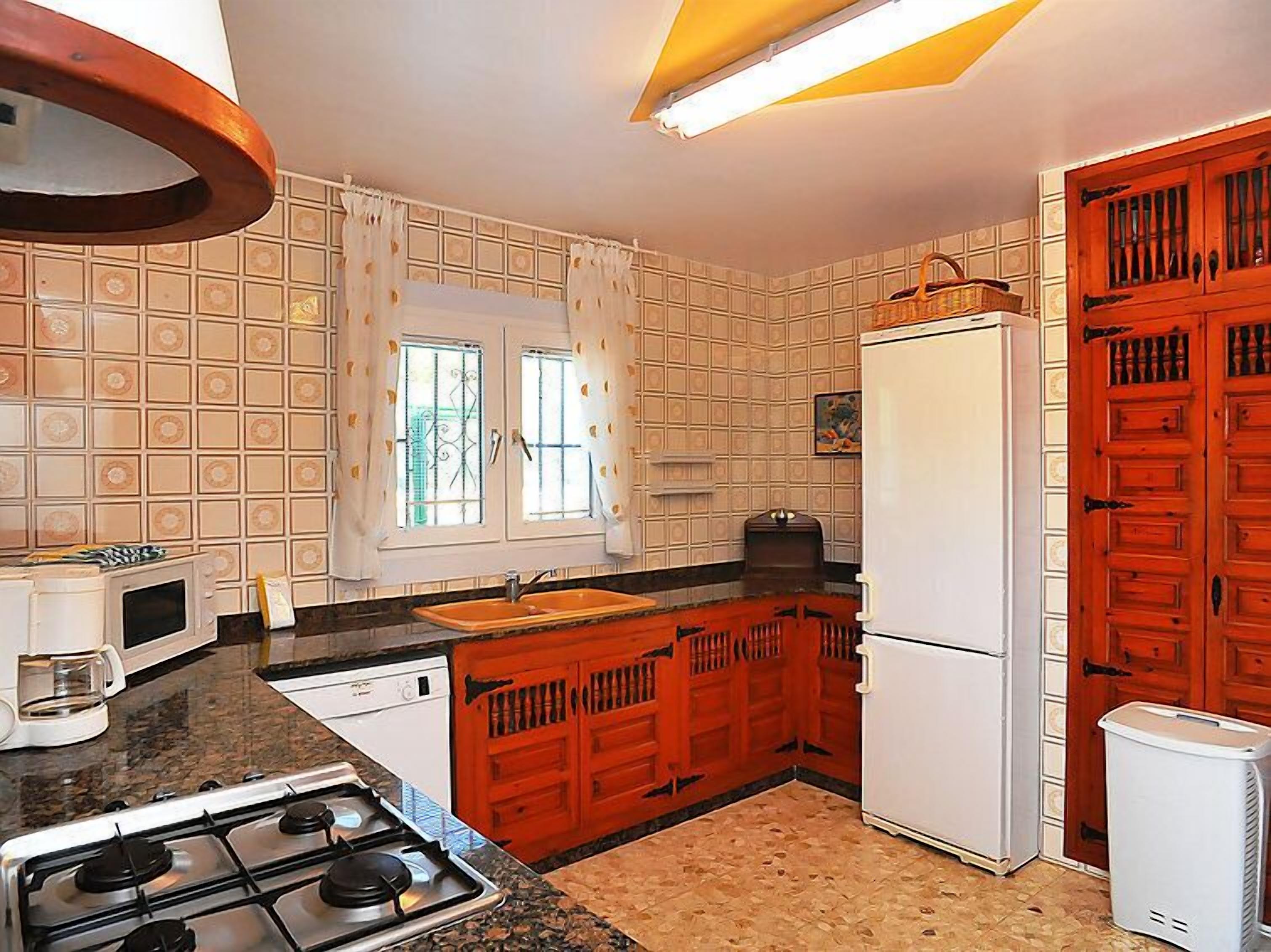 Une cuisine de taille réduite, équipée d’une cuisinière à gaz, d’appareils électroménagers blancs et d’une fenêtre avec des rideaux.