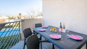 A balcony with a table set for two, featuring a bottle of wine, glasses, and a bowl of fruit.