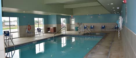 Una piscina interior con agua cristalina, paredes de azulejos y sillas azules a los lados.