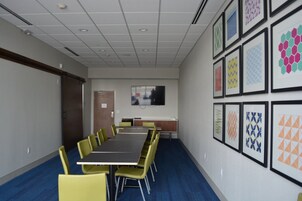 Un salón de conferencias con una larga mesa, sillas amarillas, un televisor en la pared y cuadros en la pared.