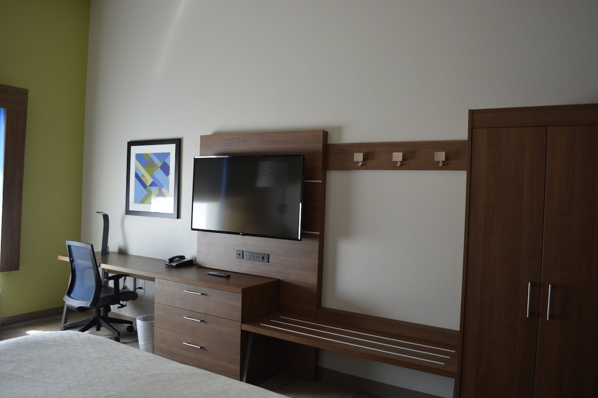 A bedroom with a bed, a desk with a computer, a chair, a television, and a wardrobe.