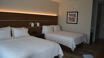 A hotel room with two beds, a nightstand, a wall-mounted light, and a framed picture.