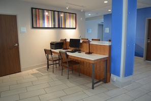 A reception desk with a computer, two chairs, and a framed artwork on the wall.