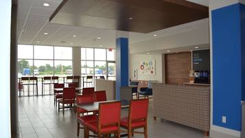 A spacious cafeteria with red chairs and tables, a coffee bar, and large windows offering a view of the parking lot.