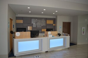 A reception desk with two computer monitors, a wooden counter, and a sign above. - Holiday Inn Express & Suites Liberal by IHG (Liberal)