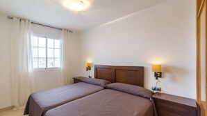 A double bed with two nightstands, a window with curtains, and a wall-mounted light fixture.