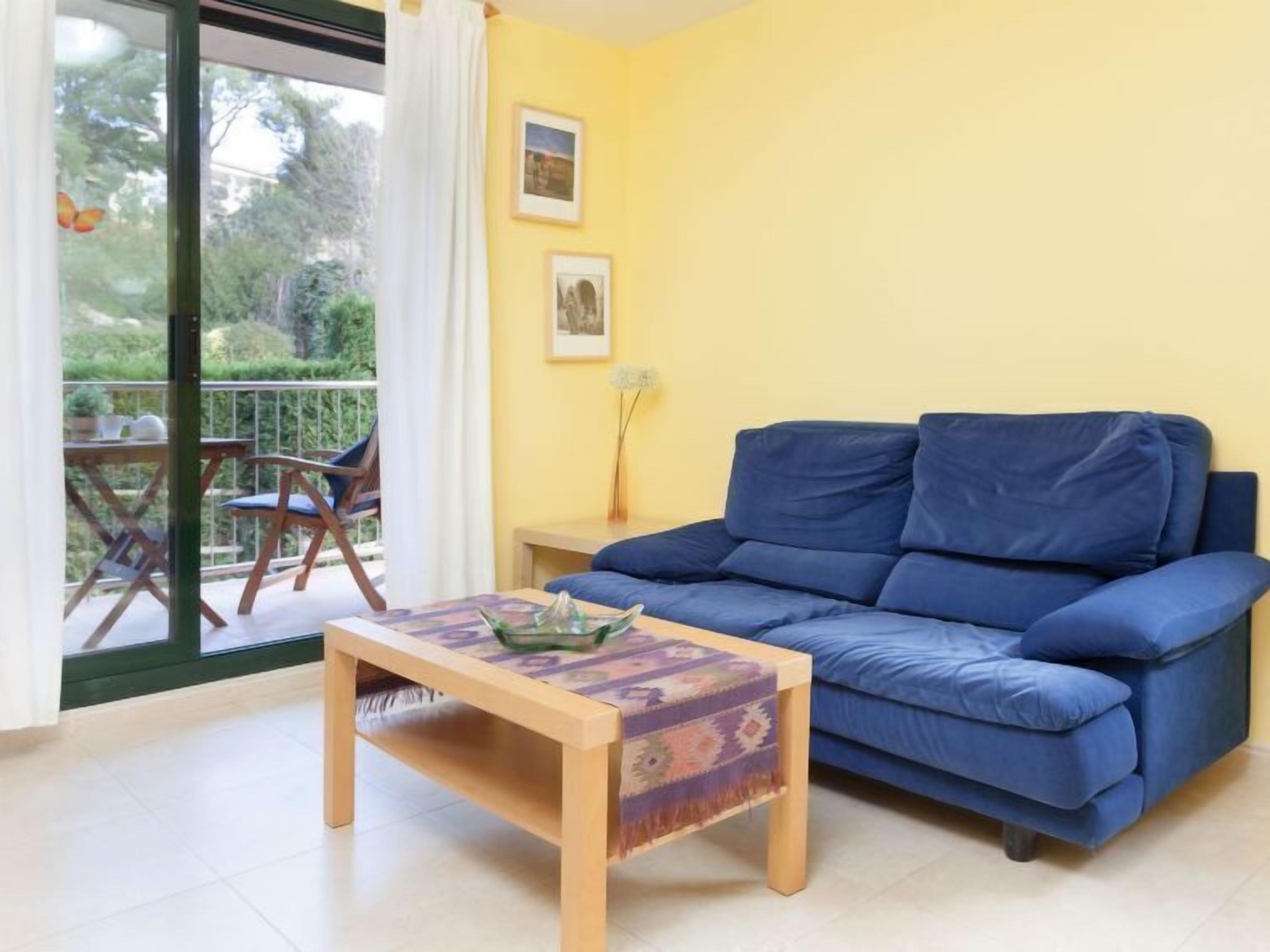A living room with a blue sofa, a wooden coffee table, and a balcony with a chair and table.