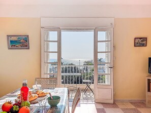 Ein Essbereich mit Tisch für zwei Personen, Blick durch eine offene Tür auf einen Balkon und ein Gemälde an der Wand.