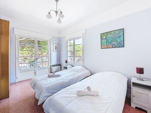 A bedroom with two beds, a ceiling fan, a painting, and a window with a view of greenery. - Les Trois A by Interhome (Saint Cyr sur mer Les Lecques)