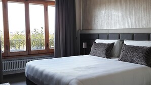 Moderni hotellihuone, jossa on suuri sänky, ikkunasta avautuva näkymä ulos ja patteri ikkunan alla.