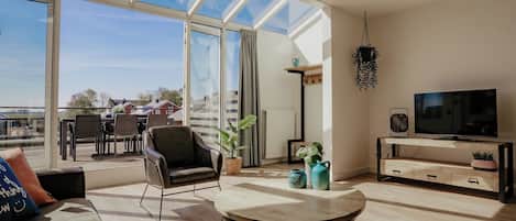A modern living room with a large skylight, a sofa, a coffee table, a TV, and a dining area with chairs and a table.