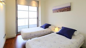 A bedroom with two beds, a sliding glass door, a cityscape painting, and a bedside lamp. - Diagonal Mar by Interhome (Barcelona)