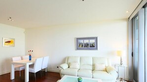 A modern living room with a white sofa, a dining table with chairs, a coffee table, and a cityscape painting on the wall. - Diagonal Mar by Interhome (Barcelona)