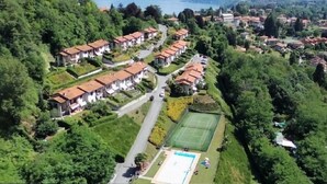 An aerial view of a residential area with houses, a tennis court, and a lake in the background. - La Rocca by Interhome (Castelveccana)