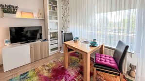 A modern living room with a flat-screen TV, a bookshelf, a dining table with chairs, and a large window with sheer curtains. - Flieder (A110) by Interhome (Lahnstein (Koblenz))
