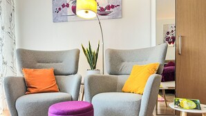 A modern living room with two grey armchairs, a purple ottoman, and a small round table with a book. - Flieder (A110) by Interhome (Lahnstein (Koblenz))