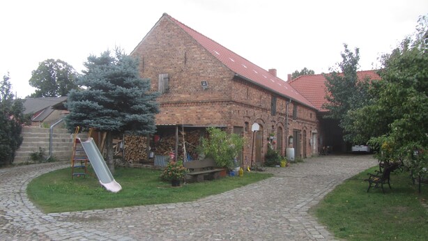 A brick building with a red roof, a stone-paved courtyard, and a slide in the yard.