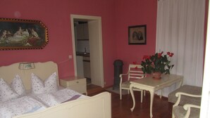 A room with a bed, a table, a chair, a potted plant, and a painting on the wall.