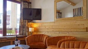 Ein gemütlicher Raum mit einer Holzwand, einem über einem Fenster montierten Fernseher und zwei bequemen, orangefarbenen Sesseln.