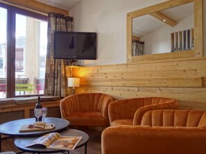A cozy room with a wooden wall, a television mounted above a window, and two plush orange chairs. - Le Grand Tichot A et B (Val Claret) by Interhome (Tignes)