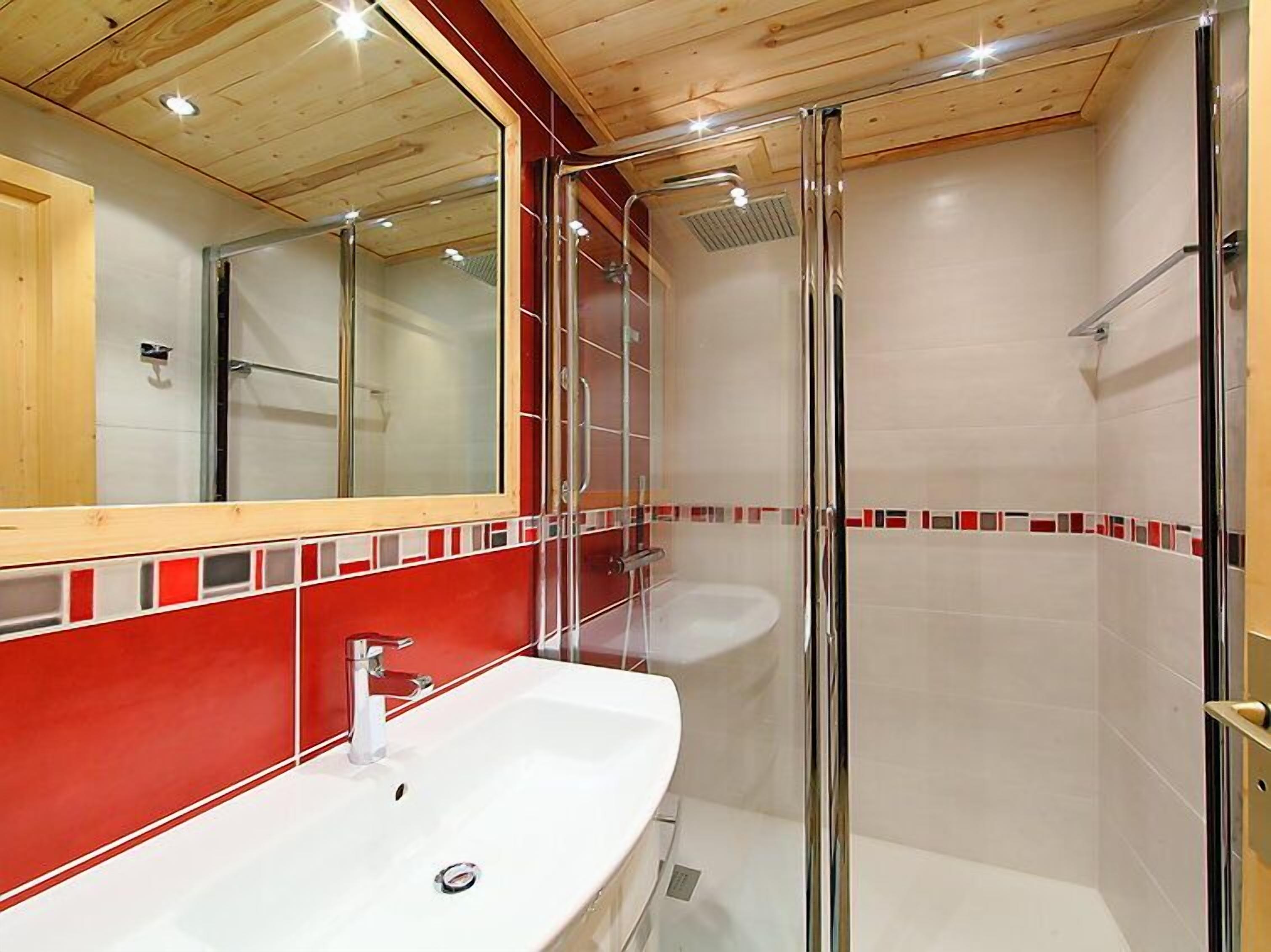A modern bathroom with a white sink, a glass shower enclosure, and a red-tiled accent wall.