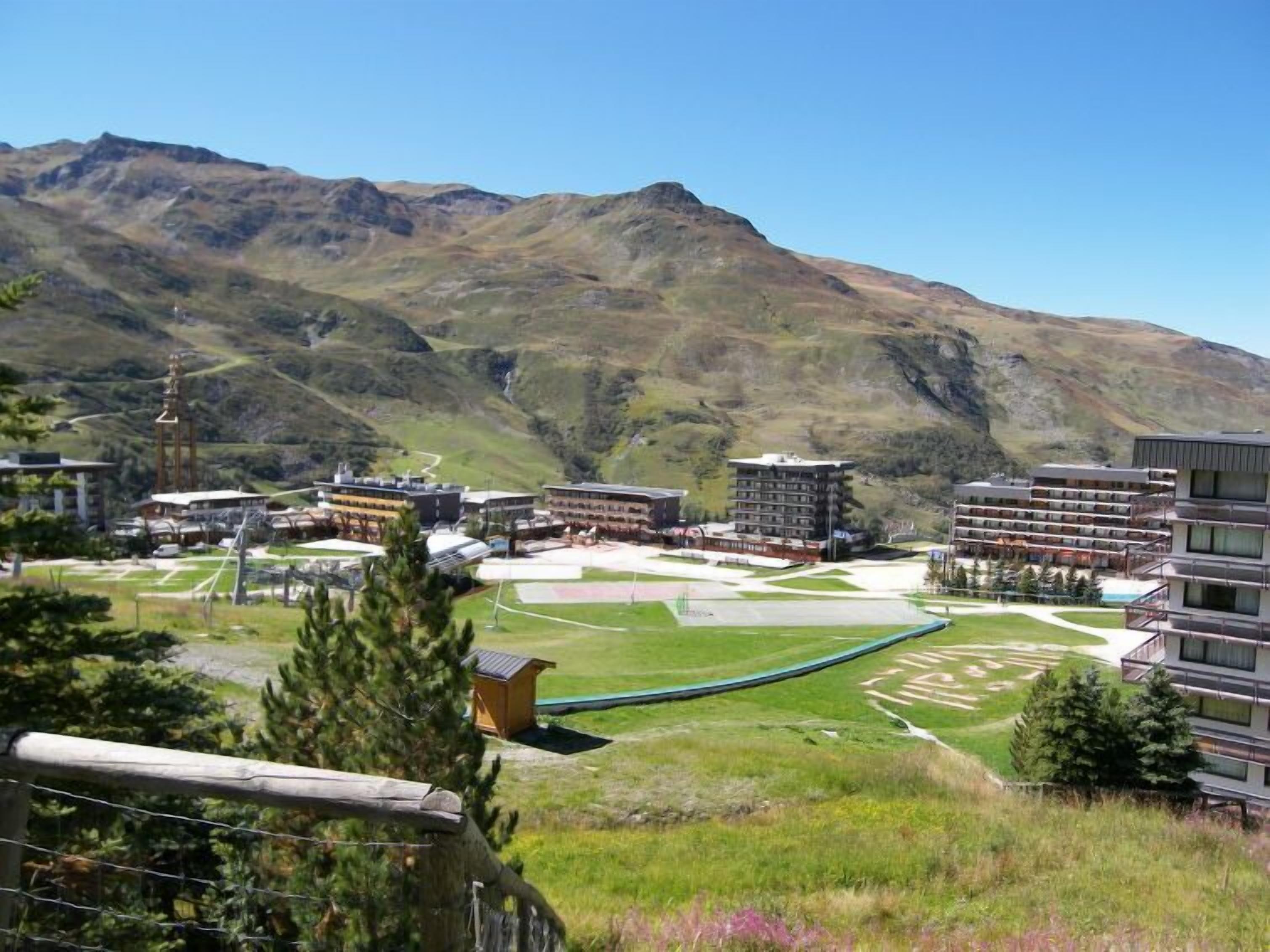 A mountainous landscape with a modern hotel featuring multiple buildings, a ski slope, and a clear sky.