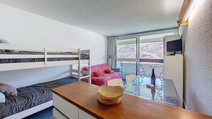 Ein Zimmer mit Etagenbetten, einem kleinen Tisch mit einem Korb, einem roten Stuhl und einem Fernseher auf einem Schrank.