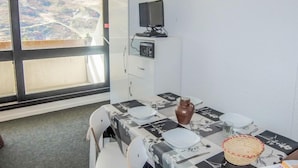 Ein gemütlicher Raum mit Esstisch für zwei Personen, einem an einem Schrank befestigten Fernseher und einem Fenster mit Blick auf eine Landschaft.