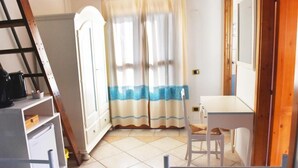 A small room with a white desk, a chair, a ladder, and a door with a curtain. - B&B Porto Frailis (Tortoli)