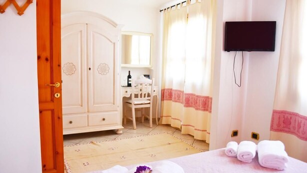 A hotel room with a bed, a desk, a chair, a TV, and a wardrobe. - B&B Porto Frailis (Tortoli)