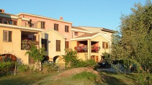 A row of Mediterranean-style buildings with balconies, a grassy area in front, and a clear sky. - B&B Porto Frailis (Tortoli)