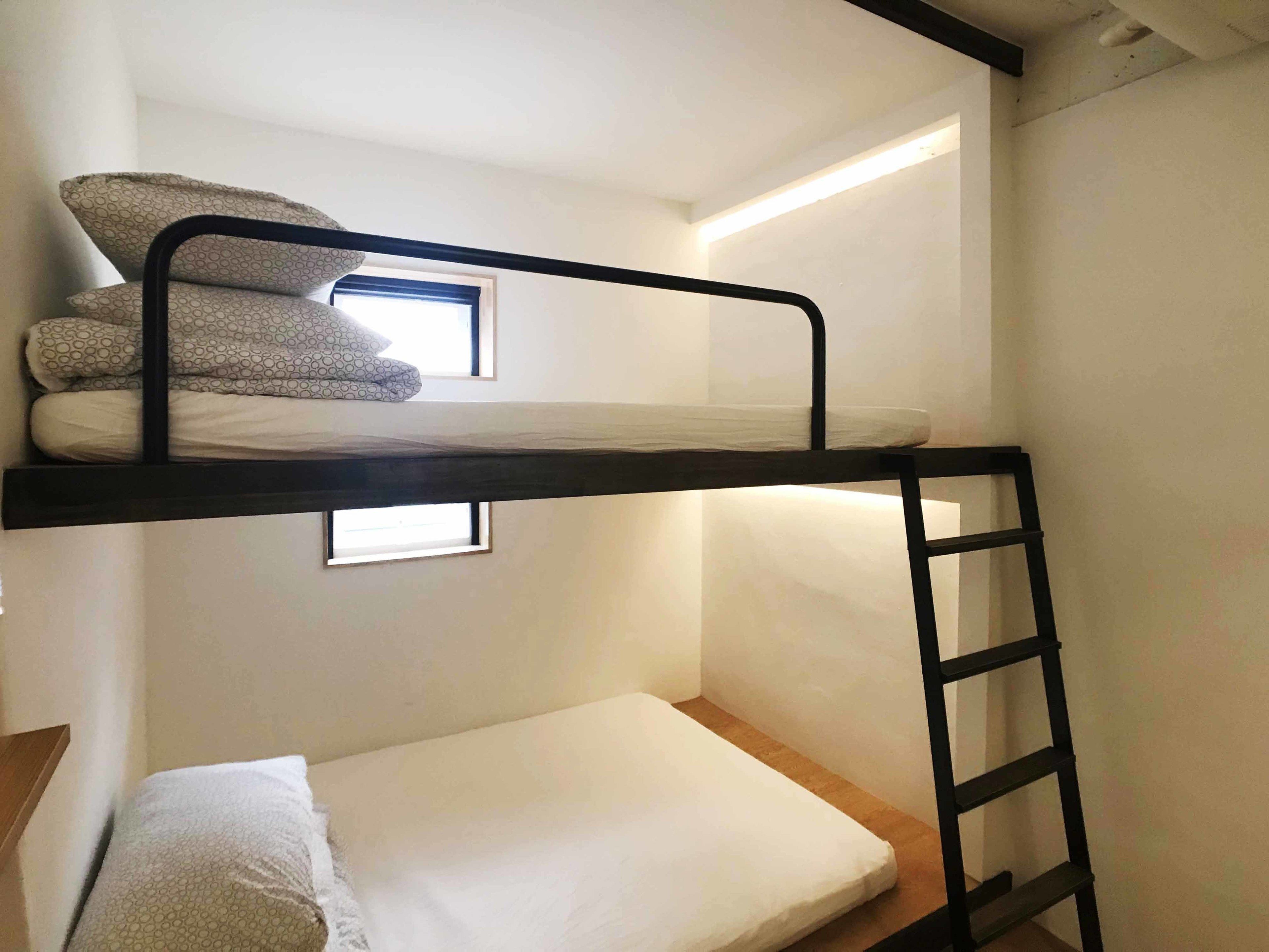 A bunk bed with a ladder, a window, and a small bedside table.