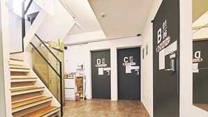 Un pasillo con una escalera, puertas negras con etiquetas y una cámara de seguridad en el techo.